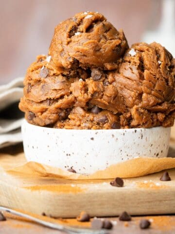 Scoops of cookie dough in a small bowl on the table with a spoon.