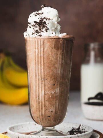 Oreo milkshake in a glass with whipped cream and crushed Oreos on top.