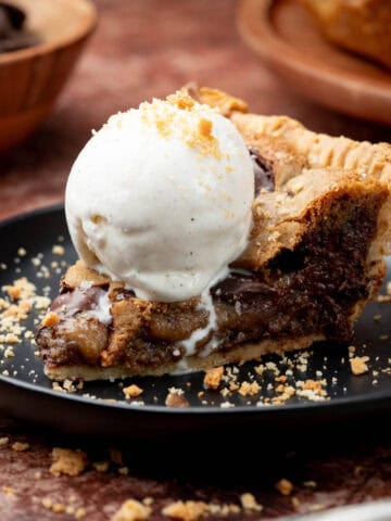 Cookie pie with ice cream on top on a black plate.