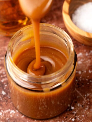 Whiskey salted caramel in a jar with a spoon and salt in the background.