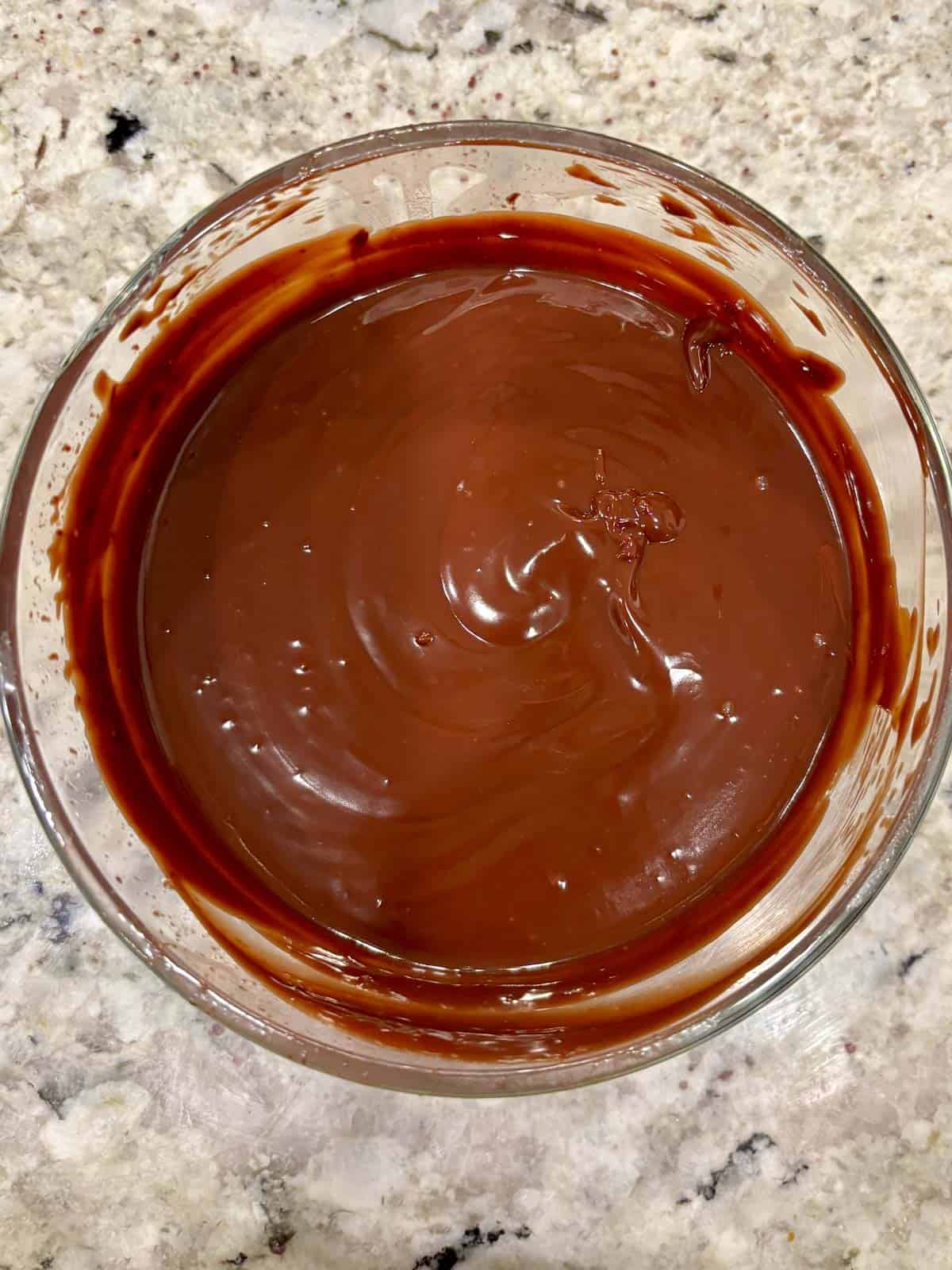 Chocolate ganache in a glass bowl on the counter.
