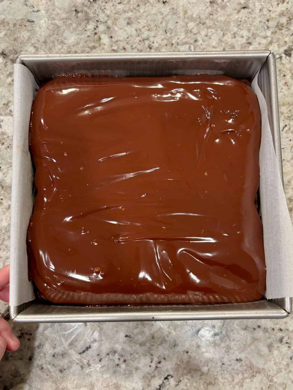 Chocolate ganache on top of chocolate cake in a metal pan.