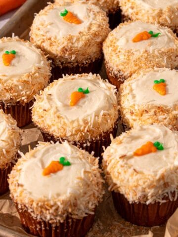 Carrot cake with coconut around the edges and mini carrots on top on a piece of parchment paper.