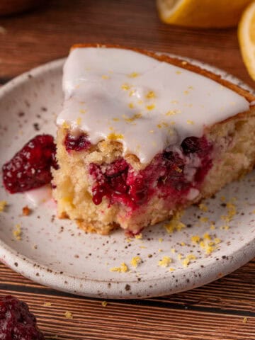 Lemon blackberry cake slice on a white plate with blackberries around and lemon zest.