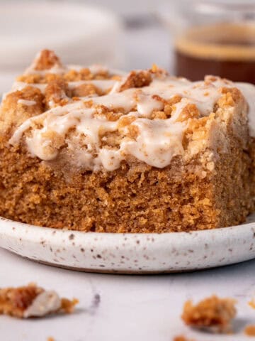 Actual coffee coffee cake slice on a plate with espresso icing on top and crumbs around it.