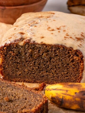 Coffee banana bread loaf with glaze on top with overripe bananas in the background.