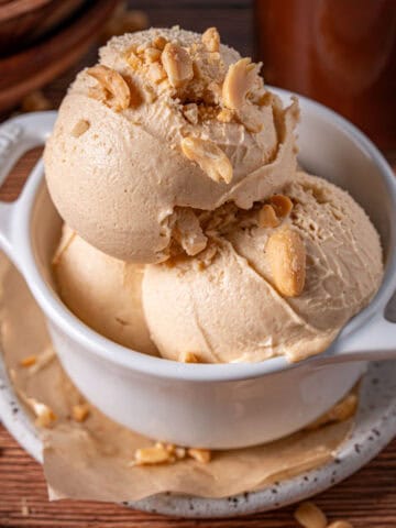 Scoops of peanut butter ice cream in a bowl with peanuts on top showing the creamy texture.